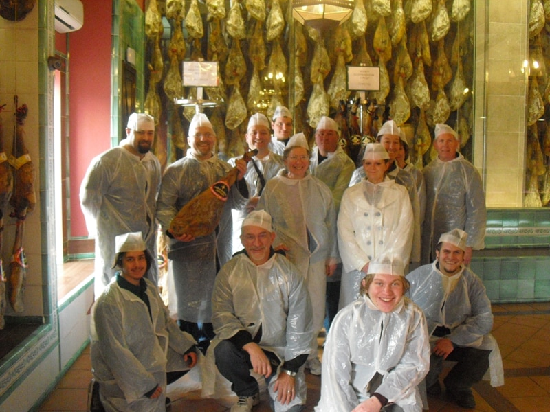 A group visiting an Iberian ham factory with hams hanging up in the background