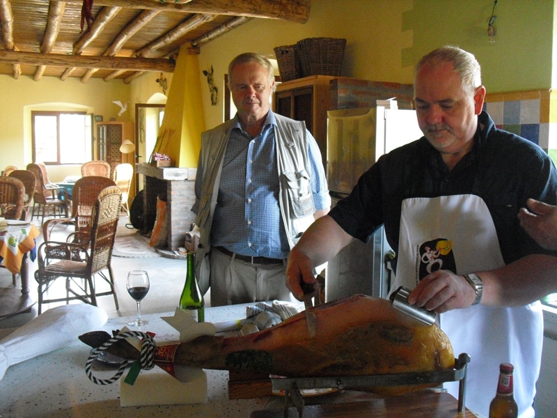 A man cutting ibercio ham with another man watching