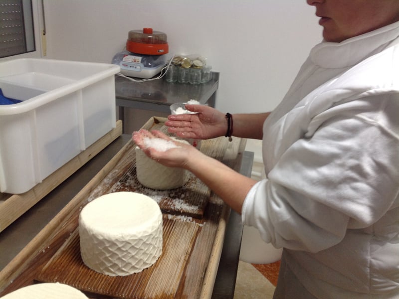 A woman is putting salt on fresh cheese